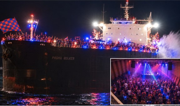 A bulk carrier lit up red and blue at night, with an inset of a packed dance floor.