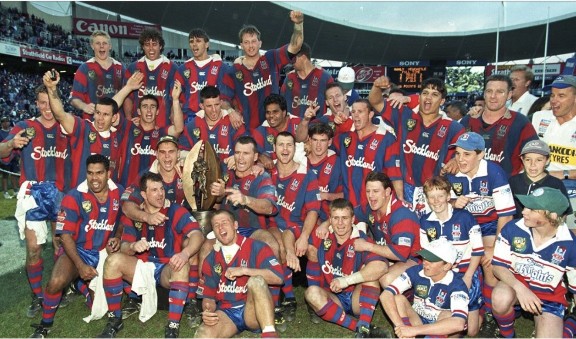 The 1997 Newcastle Knights squad celebrating on the field with the premiership trophy.
